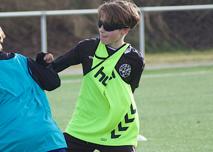 Auf dem Fußballplatz spielen 2 Jungs Fussball, beide tragen Leibchen und eine Verdunklungsbrille aus dem neurozentrierten Training Auf dem Fußballplatz spielen 2 Jungs Fussball, beide tragen Leibchen und eine Verdunklungsbrille aus dem neurozentrierten Training